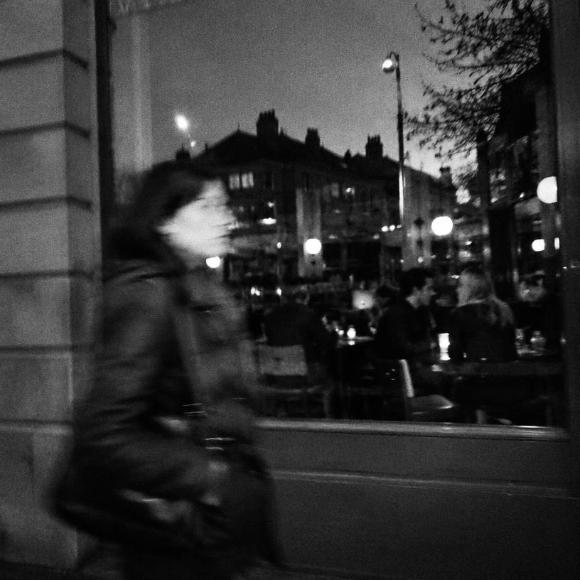 Blurred black and white street photo of a person walking past a cafe